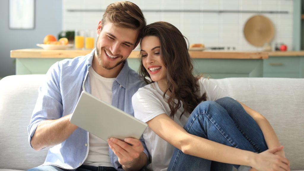 Un uomo e una donna che consultano un tablet seduti su un divano vicino alla cucina