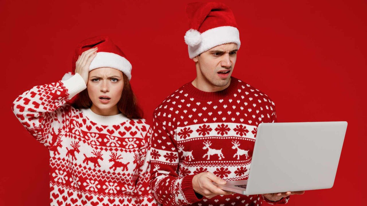 Période de Noël dans les entreprises : cinq conseils pour renforcer la sécurité des e-mails Young scared couple friends two man woman in sweater hat hold use work on laptop pc computer hold face isolated on plain red background. Happy New Year 2022 celebration merry ho x-mas holiday concept.